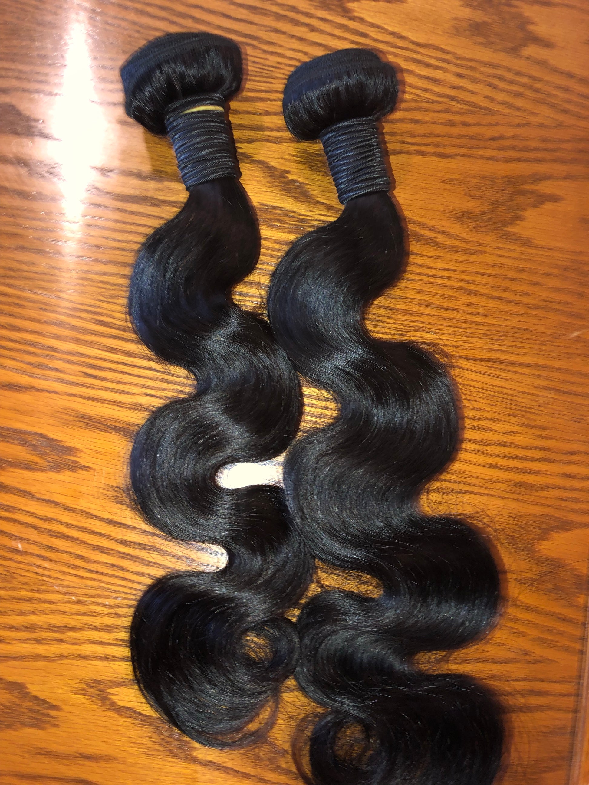 Two bundles of black hair extensions on a wooden surface
