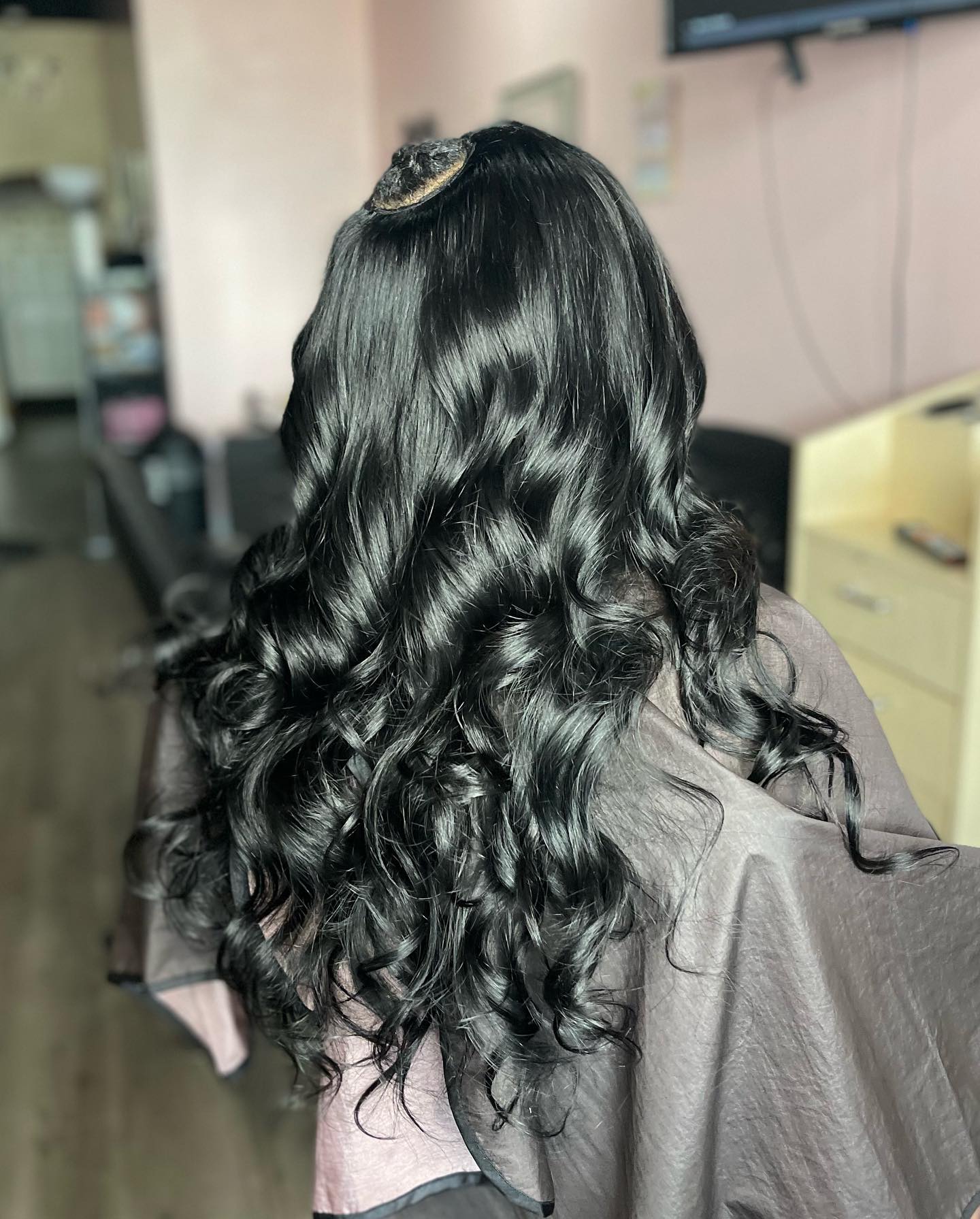 Person with long, wavy black hair in a salon setting